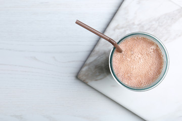 Glass with protein shake on white wooden table, top view. Space for text