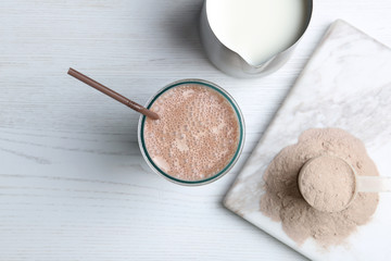 Glass with protein shake, jug of milk and powder on white wooden table, top view