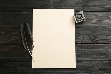 Feather pen, inkwell and blank parchment on wooden table, top view. Space for text