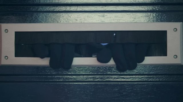 A female thief or a robber looking through a door mounted mailbox opening.