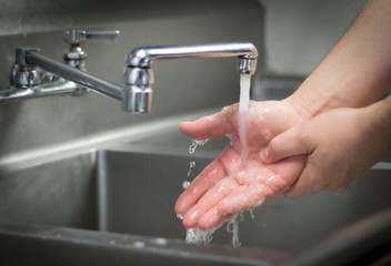 Fototapeta na wymiar Handwashing hands; washing with soap and water at stainless steel sink.