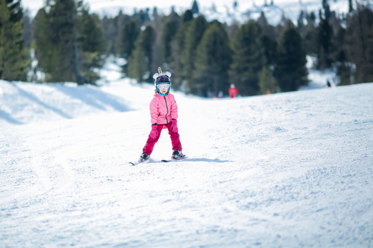 Little girl in pink ski costume skiing in downhill slope. Winter sport recreational activity