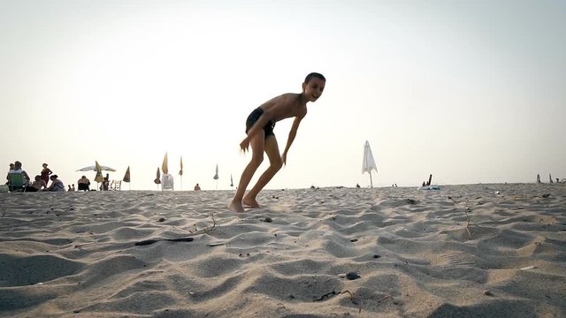 The boy runs and jumps around on the beach making catwheels in slow motion