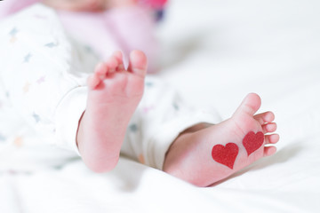 Baby foots with hearts on their feet. A newborn baby is lying on the bed.