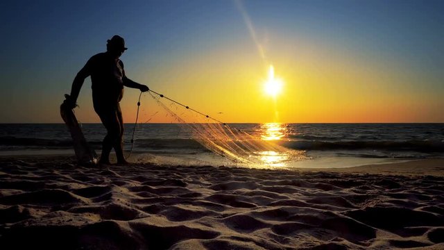 Silhouette fisherman fishing net on the sunset beach; cinematic steadicam shot