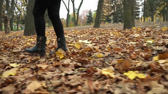 Young woman in green shoes walks on yellow leaves in the park. Autumn mood. Fresh air. Amazing holidays. Blonde young girl in a green coat. Positive emotions and happiness concept