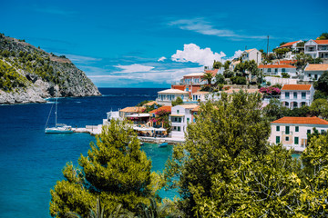 Obraz premium Wioska Assos. Piękny widok na żywe kolorowe domy w pobliżu błękitnej turkusowej przezroczystej laguny zatoki z jachtem. Kefalonia, Grecja