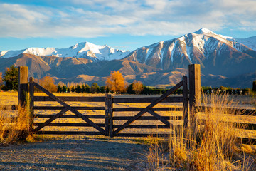 A closed wooden farm gate at the entrance to a farm in the high country below snowy mountains,...