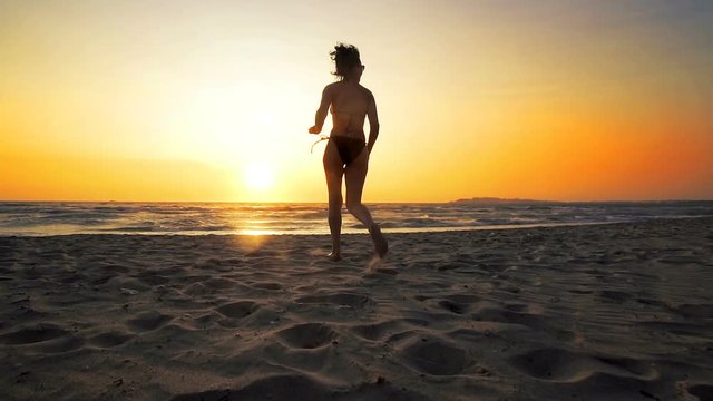 Sexy Brunette Woman with perfect Body running on the beach at sunset, cinematic SLOW MOTION