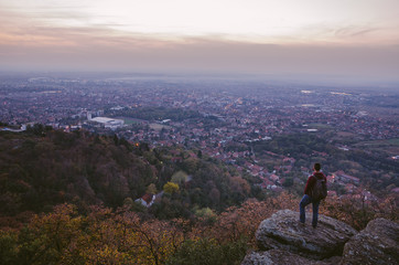 Hiker standing on the rock watching city at sunset