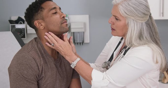 Close up of senior female doctor examining male patients neck. Portrait of attractive black male having doctor checkup at health clinic