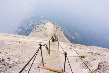 Looking down on the Half Dome cables on a summer day  smoke covering the sub dome and the valley beyond  Yosemite National Park, California