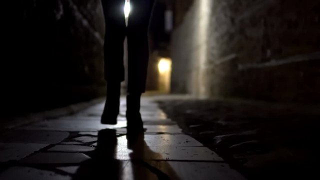 Cinematic treking of woman feet in boot walking on stone pavement in old alley dark street
