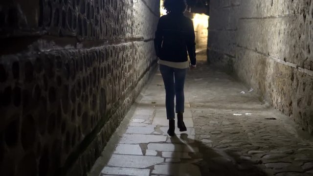 Traking a woman model walking in dark alley at night, narrow dirty corner, street in the old town