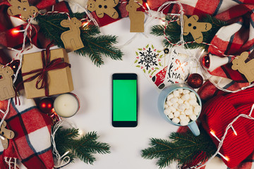 Flat lay of black smartphone with green screen on white background surrounded with Christmas...