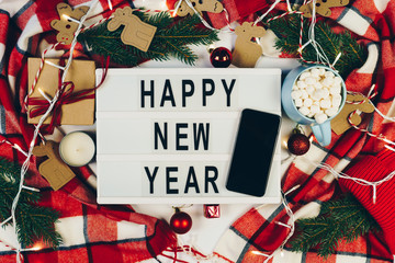 Happy New Year text displayed on a lightbox with smartphone with black screen surrounded Christmas...