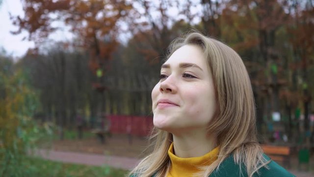 Autumn portrait of beautiful woman over yellow leaves while walking in the park in fall. Blonde young girl in a green coat. Positive emotions and happiness concept