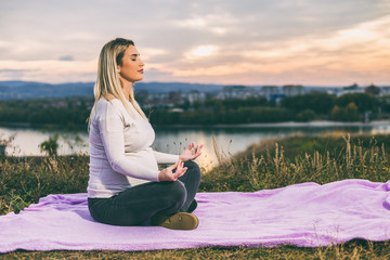 Beautiful pregnant woman enjoys meditating outdoor.