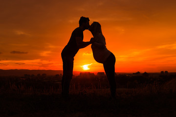 Silhouettes of husband kissing his pregnant wife into forehead and enjoy spending time together outdoor.
