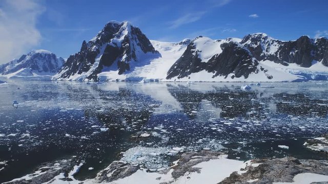 Aerial Flight Over Antarctica Ocean. Snow Mountains Background. Drone Shot Of Lemaire Channel. Clear Ocean Water Surrounded By Snow Covered Rocks, Mighty Mounts. Stunning Winter Landscape. 4k Footage.