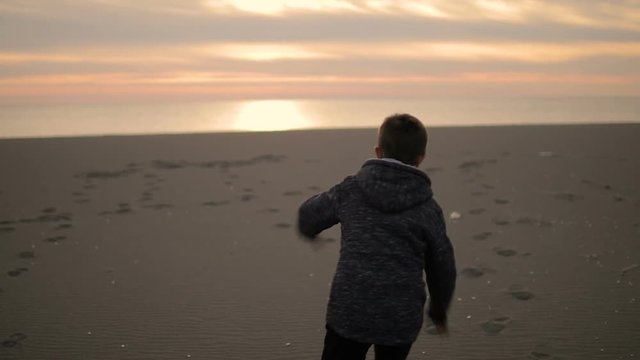 The boy walks along the beach at sunset.