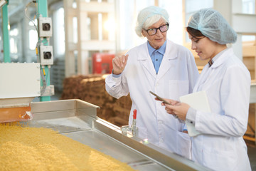 Waist up portrait of senior factory manager talking to young worker during quality inspection  in...