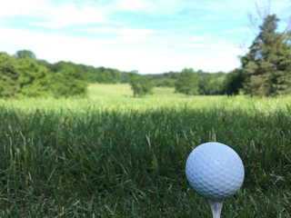 White golf ball sits on a tee ready to be hit by club down the fairway of a beautiful generic golf course on a sunny day