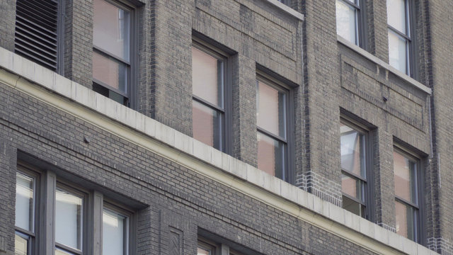 Establishing shot of generic brick facade building day DX photo. Tight tilt up office apartment windows in city