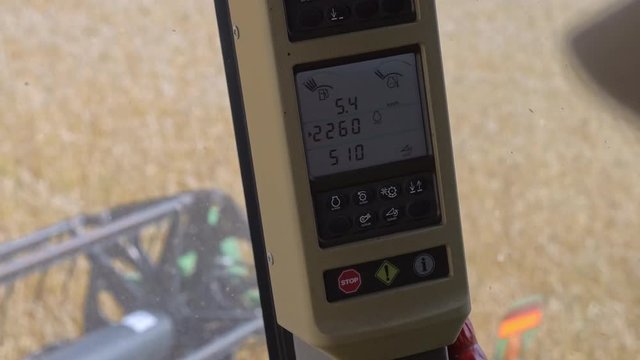 Modern harvesting tractor controlling panel close up in the cab. View from inside machine to the agricultural golden field. Working process combine harvester. Professional harvest manufacturing