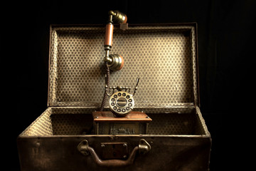 Vintage background. Very old suitcase and telephone isolated on black.