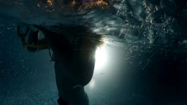 Little girl silhouette swimming underwater toward light in dark pool