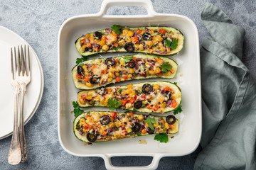 Stuffed zucchini boats with vegetables ( tomato, pepper, corn, red onion and olives) and cheese in white baking dish