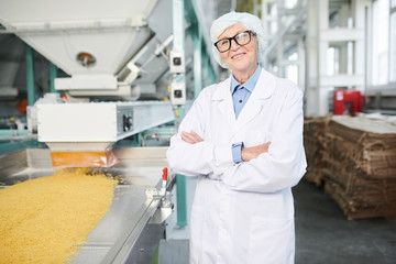 Waist up portrait of  smiling senior woman working at factory and posing cheerfully  standing by...