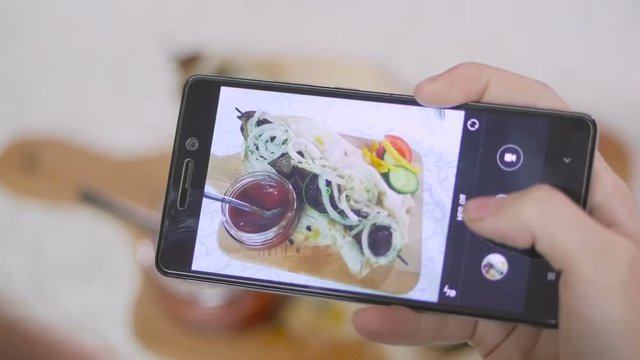 Female hands are taking an appetizing meat dish on a smartphone in a restaurant.