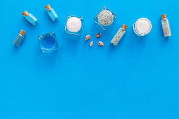 Dead sea cosmetics layout. Sea salt in bottles and bowls near small shells on blue background top view copy space