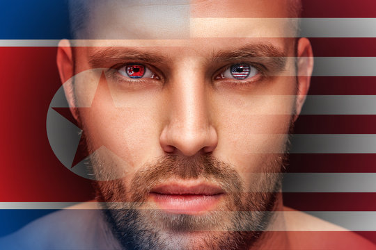 Portrait of a young serious man, in whose eyes the reflected national flag of Korea and America, against an isolated black background and flag