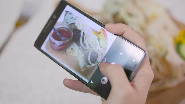 Female hands are taking an appetizing meat dish on a smartphone in a restaurant.