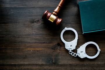 Crime concept. Metal handcuffs near judge gavel and law book on dark wooden background top view...