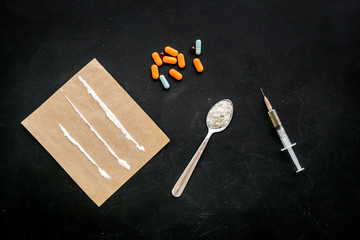 Take drugs, drugs addiction concept. White powder like heroine or cocaine, drug tracks pills, spoon, syringe on black background top view