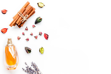 Perfume with bright fruity, floral, spicy fragrance. Ingredients for perfume. Bottle of perfume near dry flowers, cinnamon and candles on white background top view pattern copy space