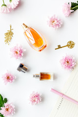 Perfume on feminine desk. Women's accessories. Perfume near notebook for dairy, vintage key among flowers on white background top view