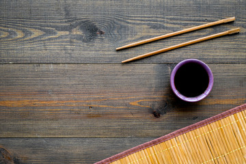 Chinese meal concept. soy sauce in bowl near chopsticks and bamboo table mat on dark wooden background top view copy space pattern