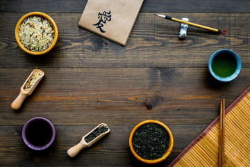 Chinese traditional symbols concept. Tea, rice, hieroglyph symbol, bambootabe mat, chopsticks, soy sause on dark wooden background top view frame copy space
