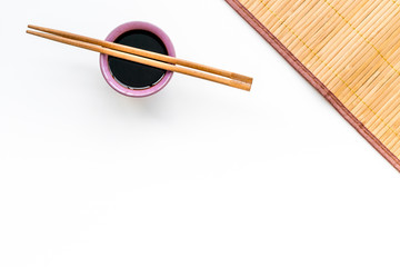 Chinese meal concept. soy sauce in bowl near chopsticks and bamboo table mat on white background...