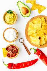 Popular mexican snack nachos. Tiangle nacho tortilla near salsa and guacamole sause, chili pepper, salt on white background top view