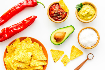 Popular mexican snack nachos. Tiangle nacho tortilla near salsa and guacamole sause, chili pepper, salt on white background top view