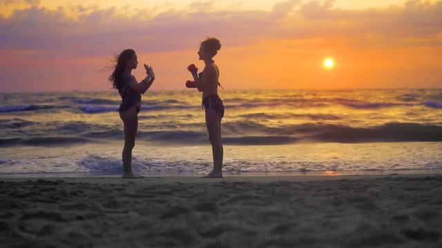 Two girls exercise, training karate on ocean beach against sunset sky and rolling waves, SLOW MOTION
