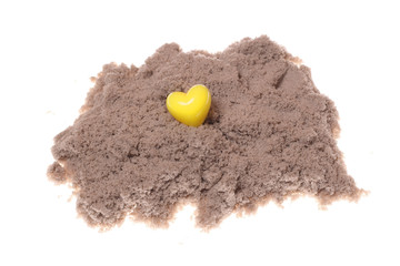 Yellow plastic heart on the sand on a white background. Isolated photo.