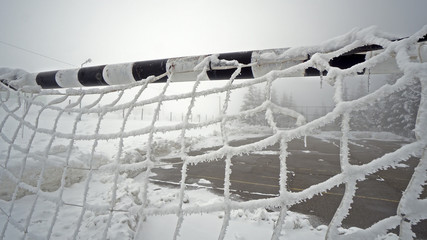 View of empty soccer and handball center court and goal with net covered with snow during winter