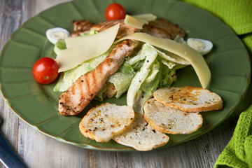 Fresh caesar salad in a green plate on a light wooden table